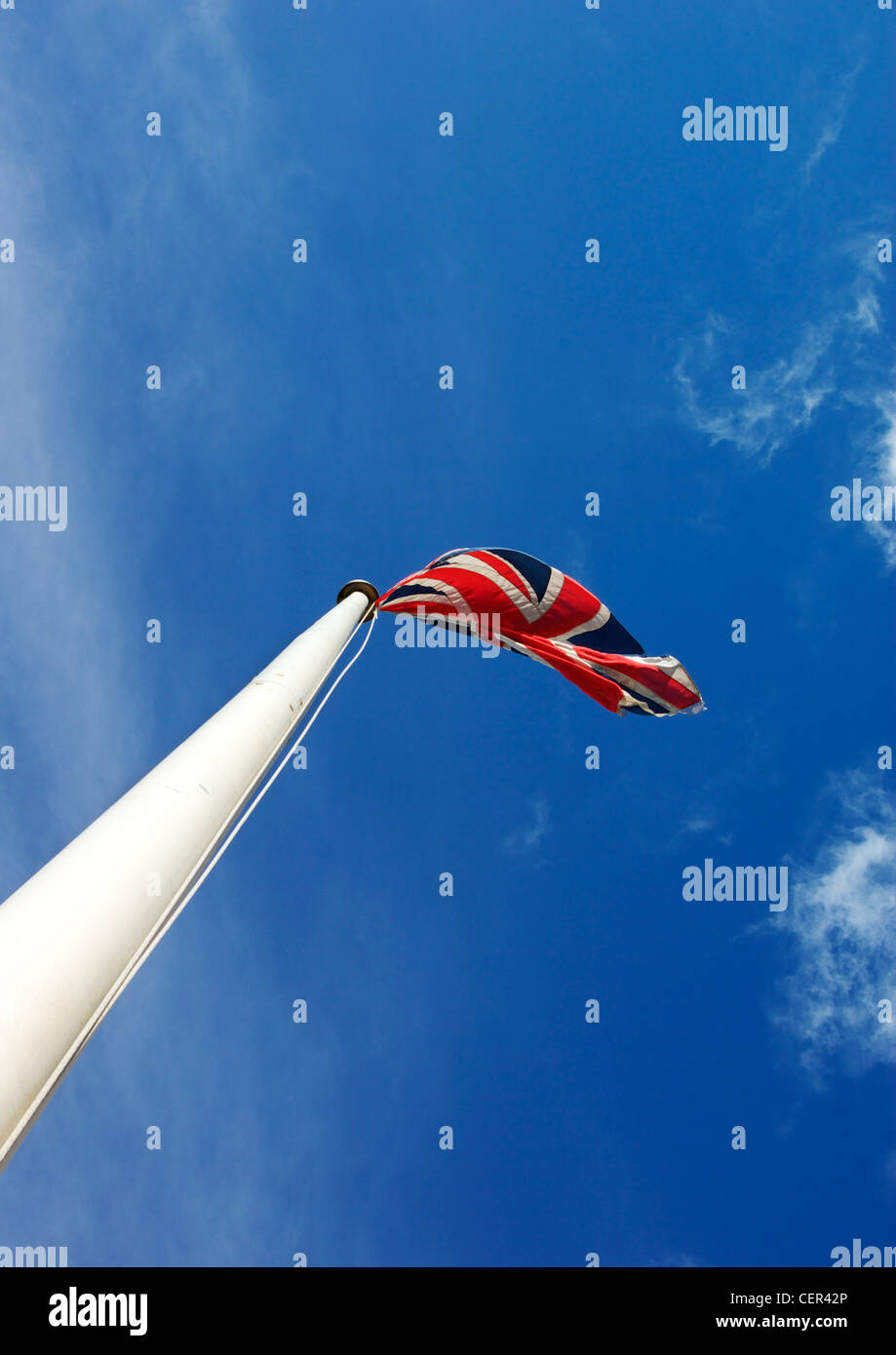 Union Jack flag on a white pole against a blue sky. Stock Photo