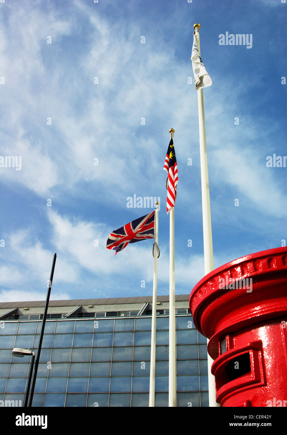 Red pillar box beside three flag poles. Stock Photo