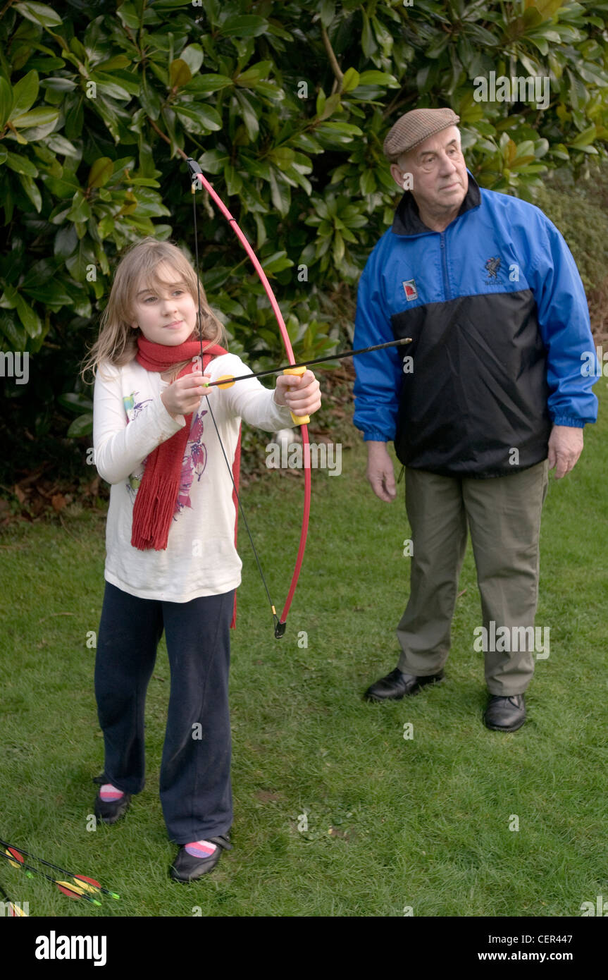 A  9 year old girl plays with a bow and arrow overseen by her grandfather Stock Photo