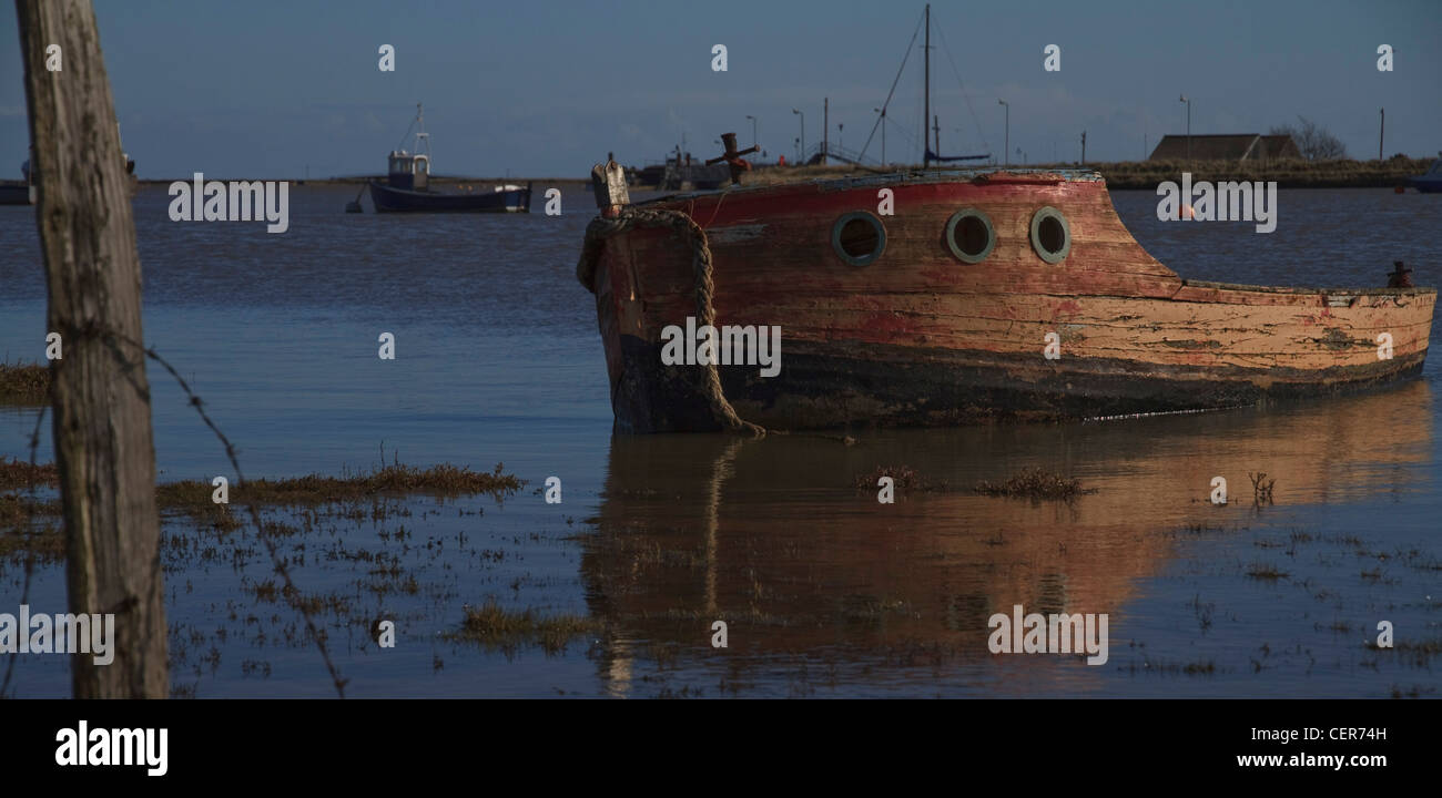 An old, abandoned boat in the harbour at Orford, Suffolk, England, with Orford Ness in the background Stock Photo