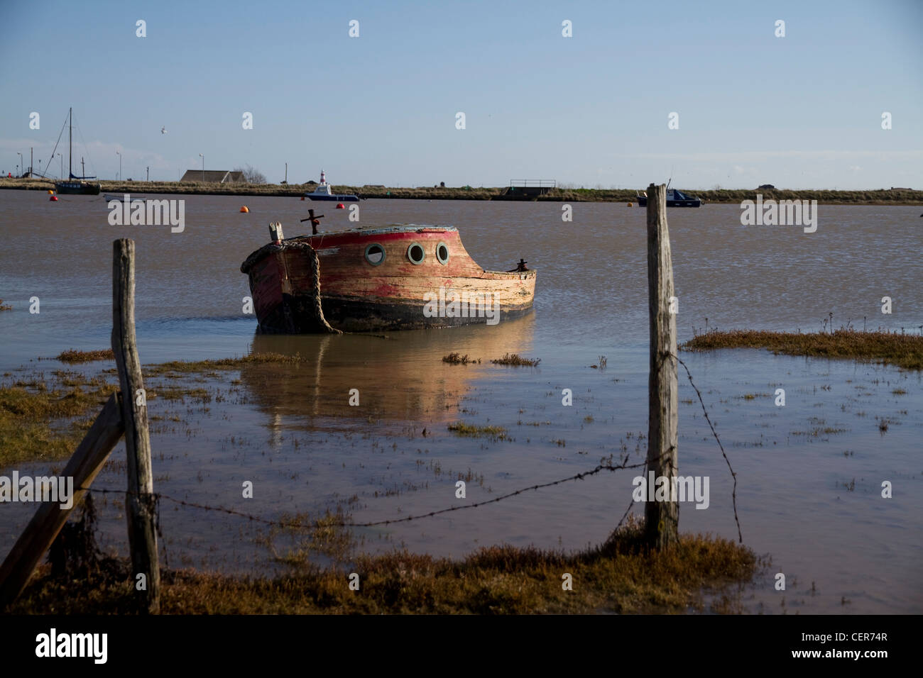 An old, abandoned boat in the harbour at Orford, Suffolk, England, with Orford Ness in the background Stock Photo