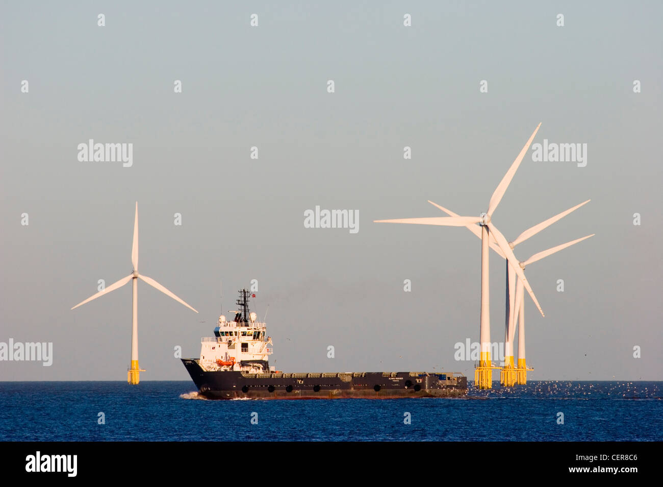 A cargo ship, the Olympic Provider passing in front of an offshore wind farm at Great Yarmouth in Norfolk. Stock Photo