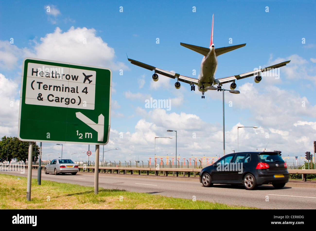 Cars on the A4 passing a road sign for Heathrow airport as a plane comes into land directly overhead. Stock Photo