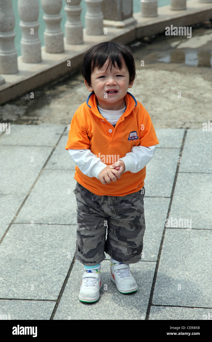 Chinese Eurasian baby Boy look at camera. He is cute and wears orange top  and military trouser. He just stand straight, alone Stock Photo - Alamy