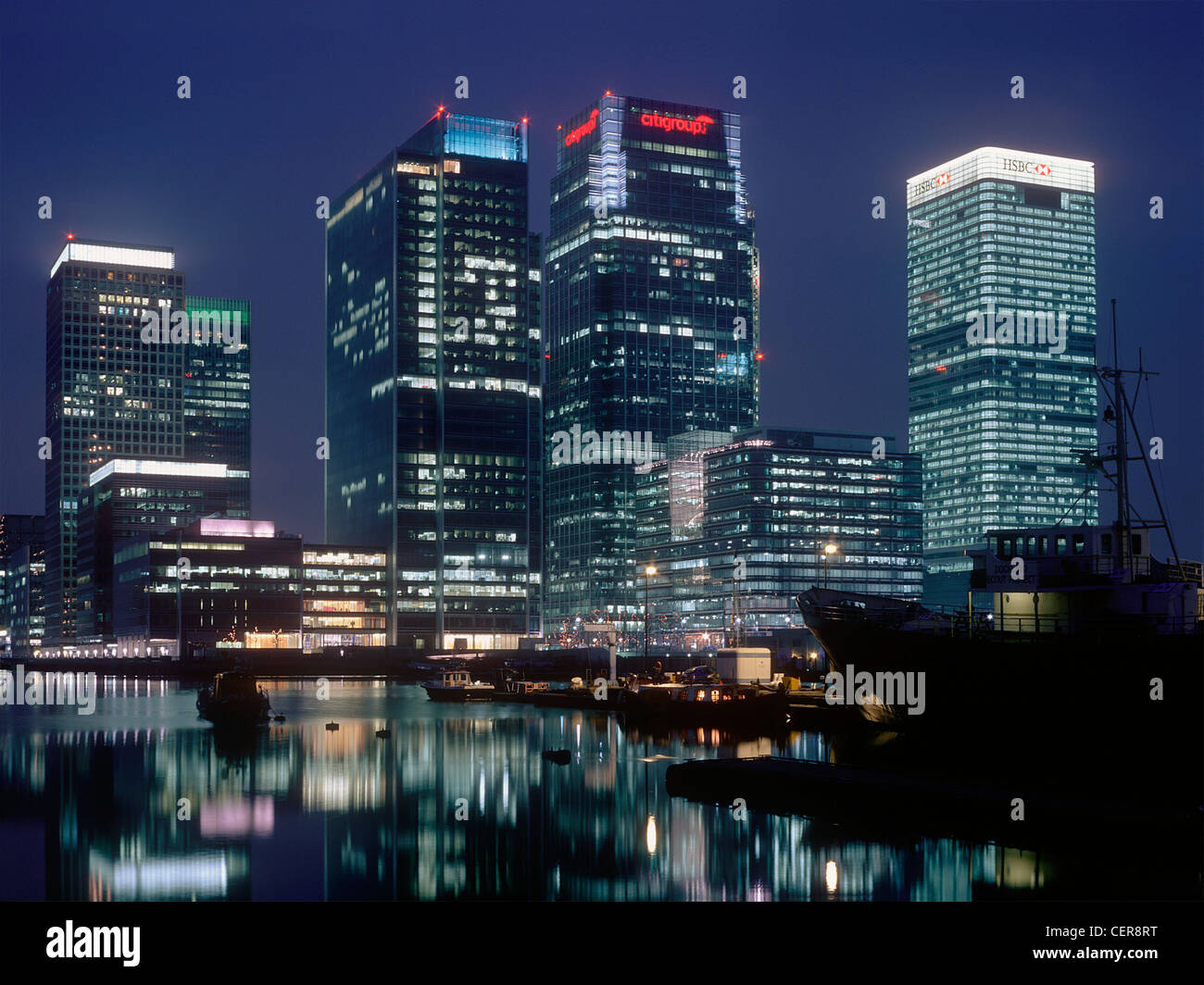 Office blocks reflected in the waters of the West India Docks at night. Canary Wharf is home to three of the tallest buildings i Stock Photo