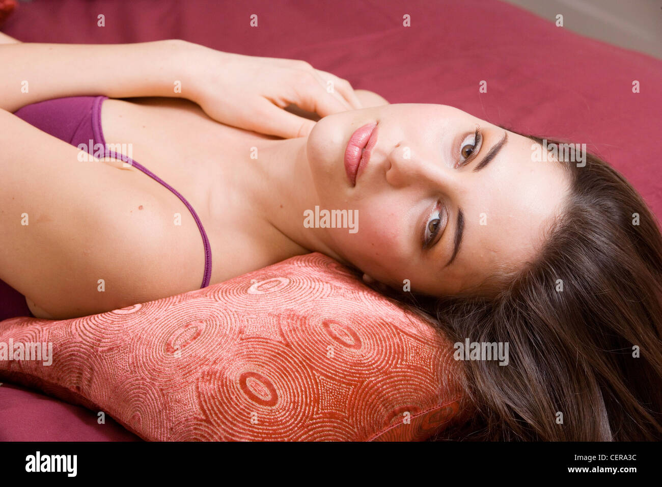 Winter Lifestyle Female long brunette hair laying on her back on a bed a red duvet, head propped on a red pillow, hair flowing Stock Photo
