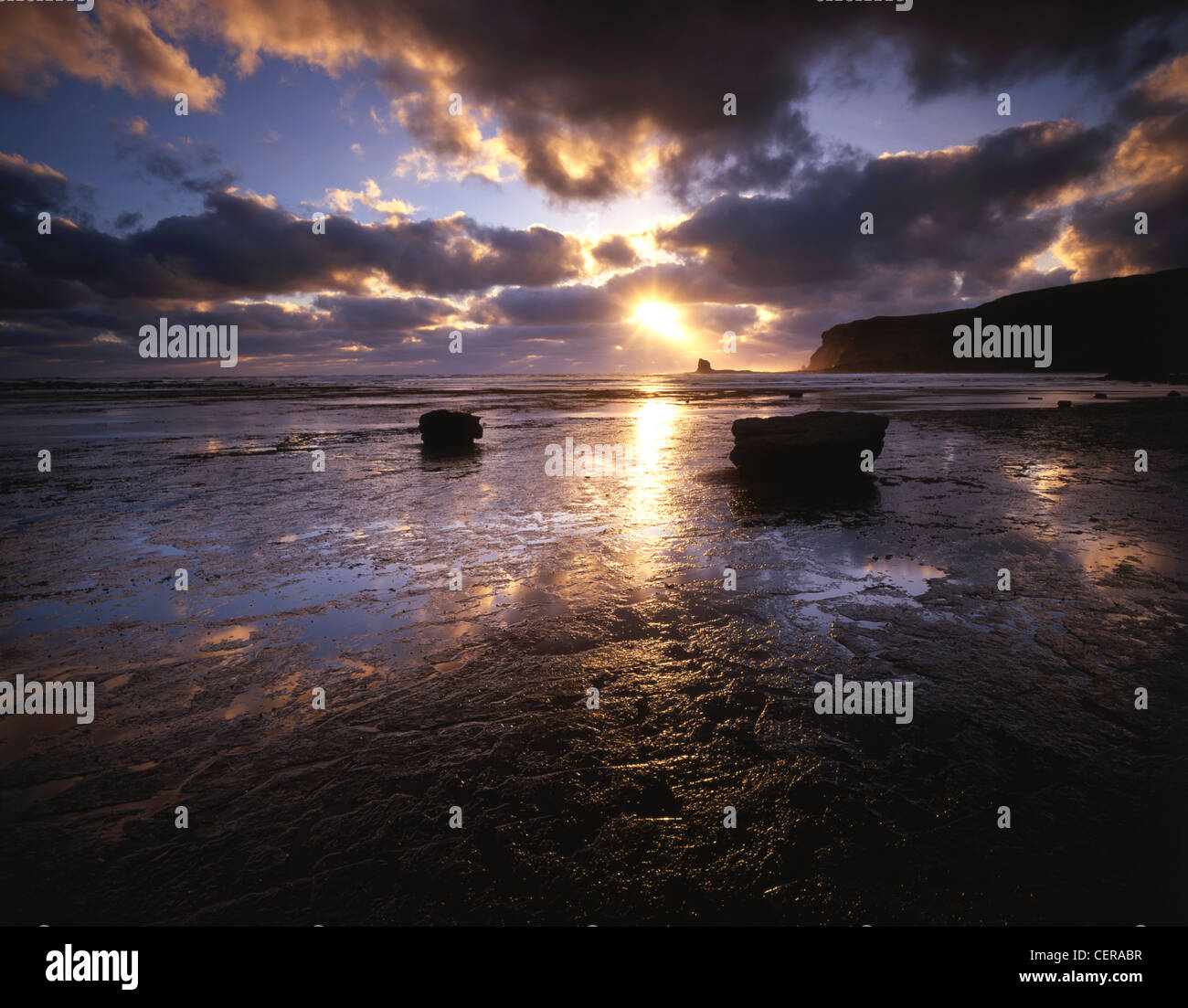 A dramatic sunrise on the rock platform at Saltwick Bay near Whitby. Black Nab can be seen below the sun. Stock Photo