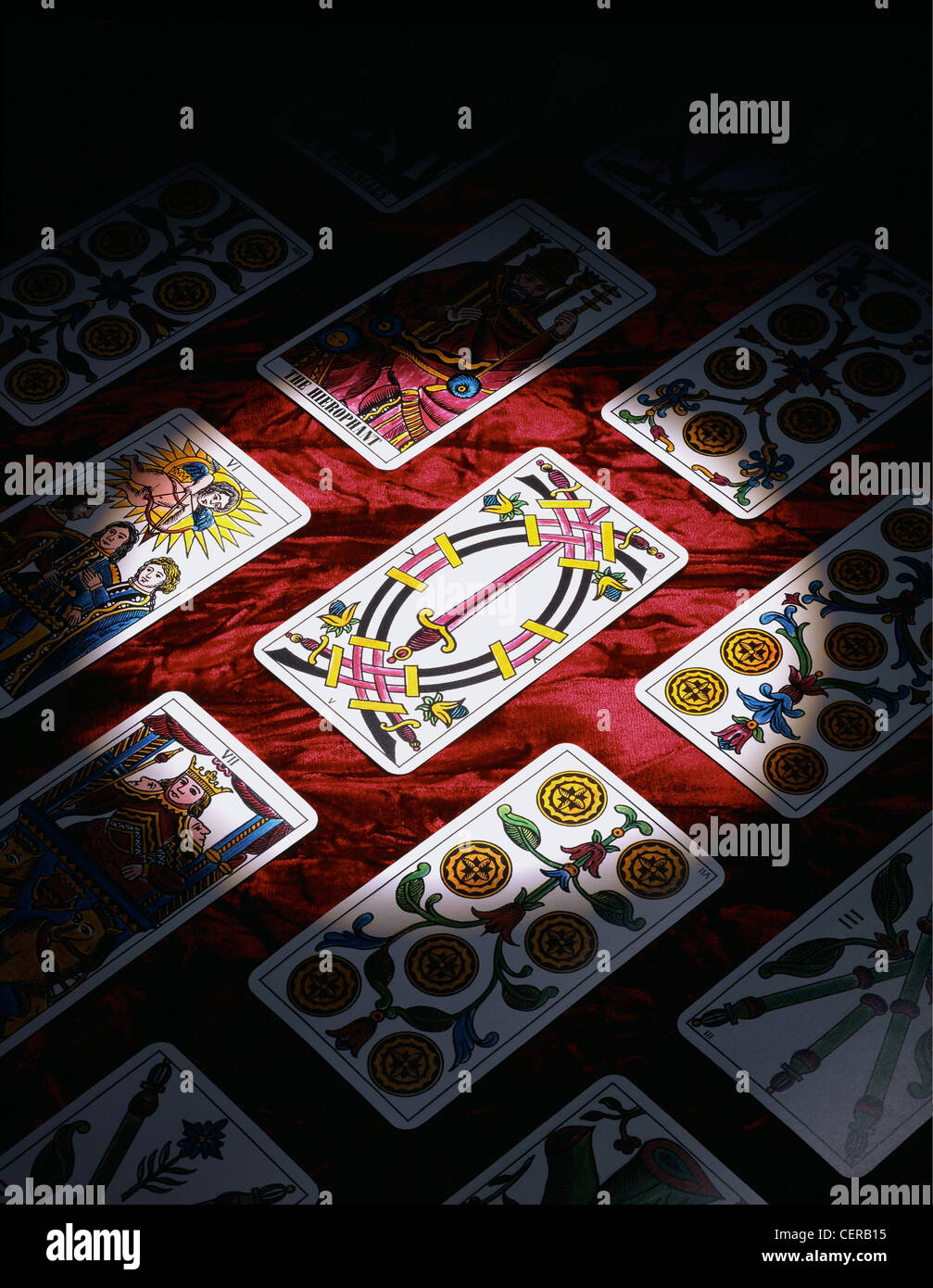 Tarot Cards laid out in rows on a red patterned background, partially lit by a spotlight Stock Photo