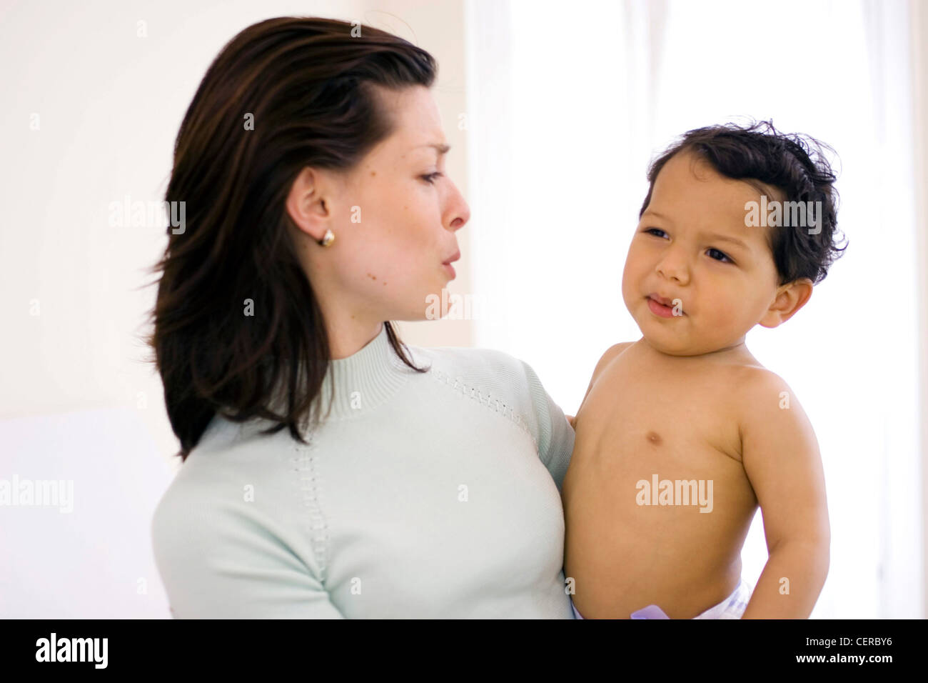 Female with brunette hair looking sideways at and holding male child in arms both pursing lips Stock Photo