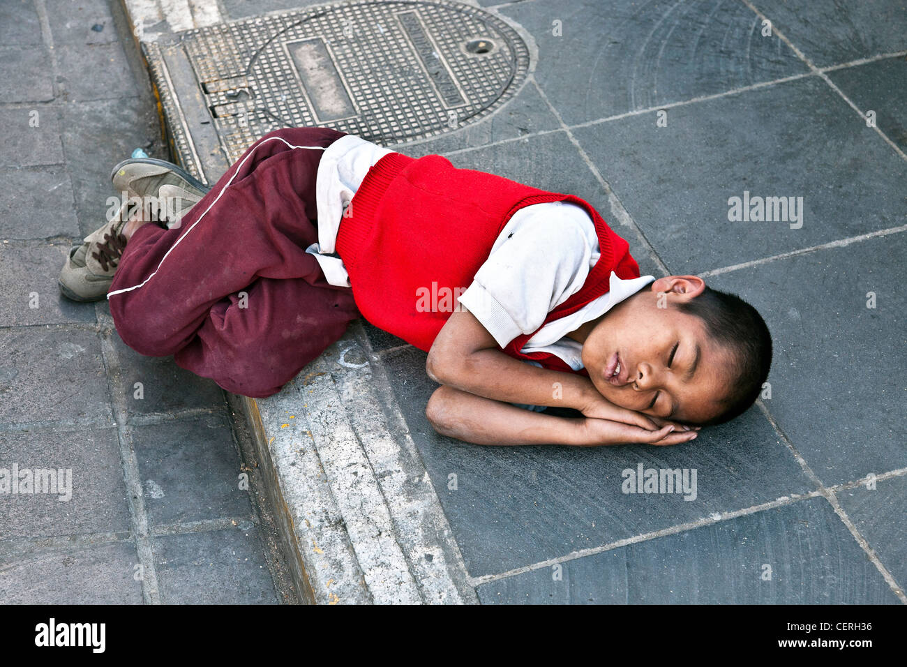 tired young Mexican schoolboy in red school sweater fast asleep on paving stones Oaxaca Zocalo Mexico Stock Photo