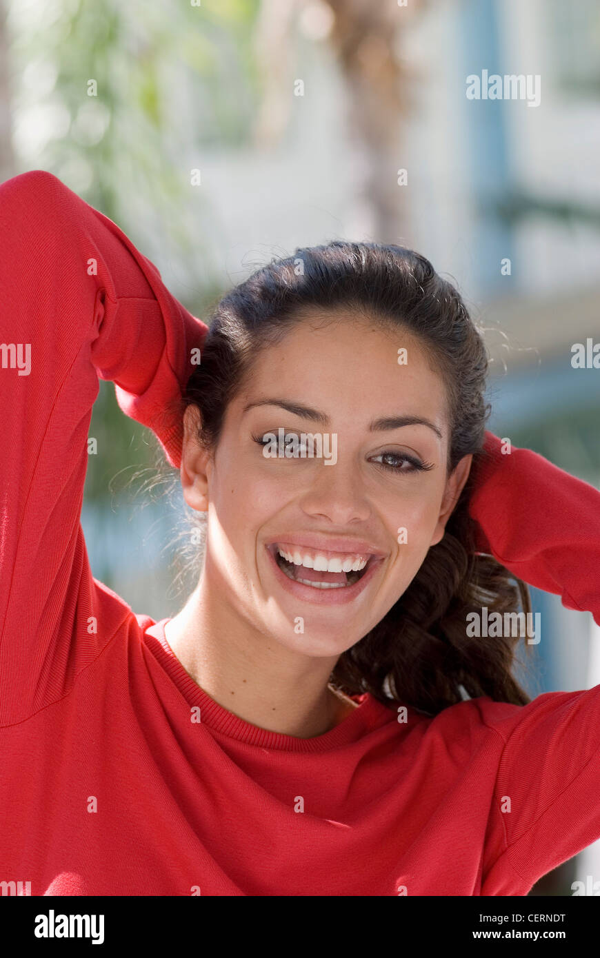 Female wearing red jumper, hands on back of head, smiling to camera