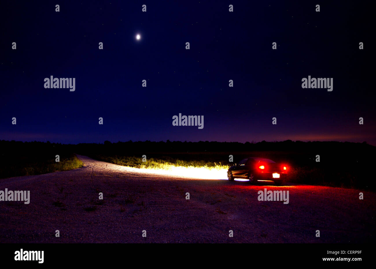 A car parked at the side of the road under the moon. Stock Photo