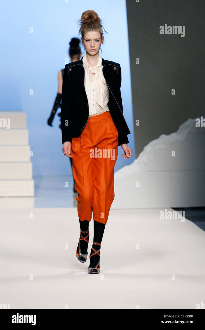 Sportmax Milan Ready to Wear Autumn Winter Model wearing orange cropped trousers, white blouse tie detail and black military Stock Photo