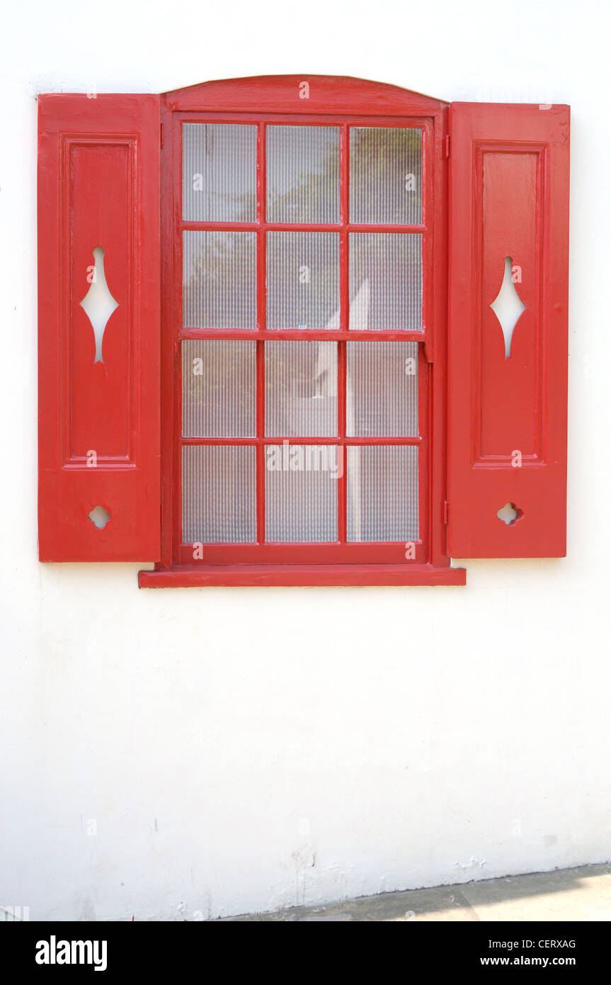 Sash window on white house painted bright red with shutters with cut out diamond shape detail Stock Photo