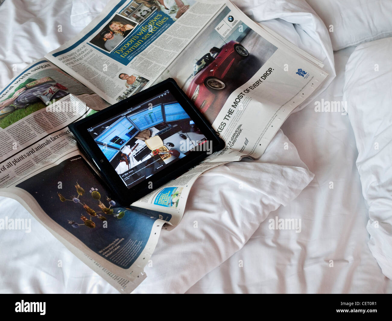 Apple iPad with sunday papers on unmade bed Stock Photo