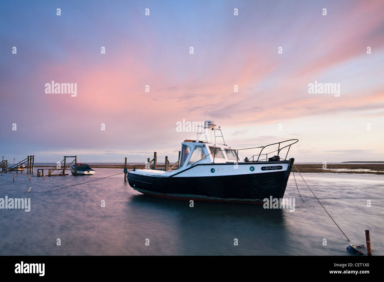 Boats moored in Thornham Harbour by the remains of an ancient wooden pier at high tide on the North Norfolk Coast. Stock Photo