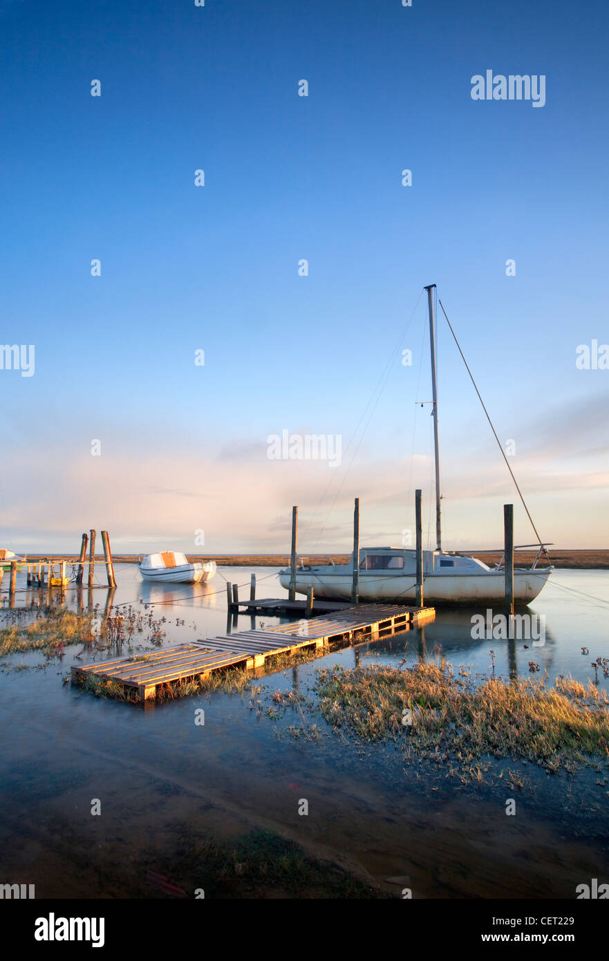 Boats moored at Thornham Harbour by the remains of an old pier at first light. Stock Photo