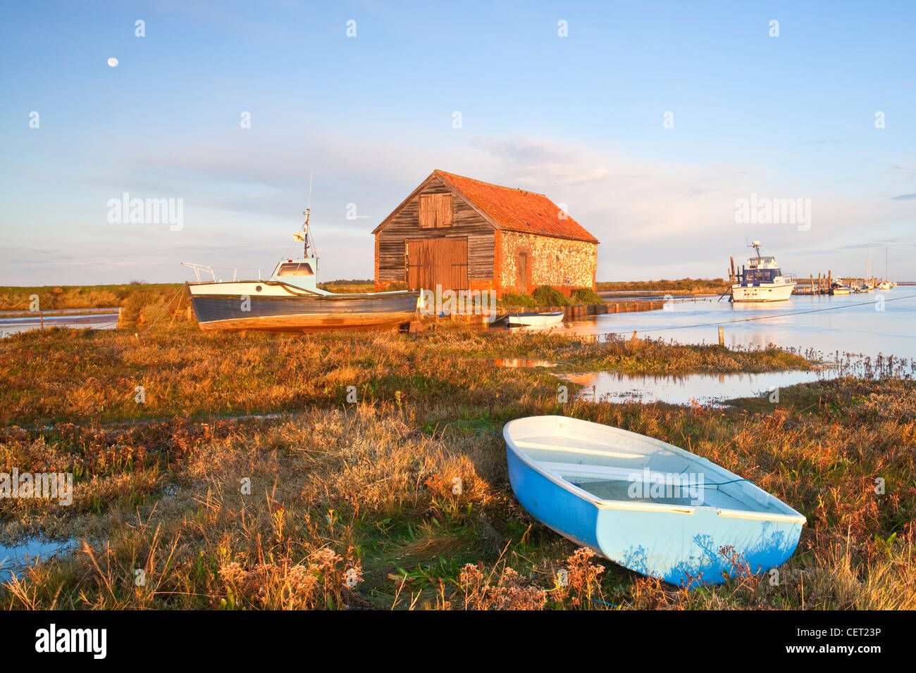 Boats and the old coal shed at first light at Thornham Harbour during a high tide on the North Norfolk Coast. Stock Photo