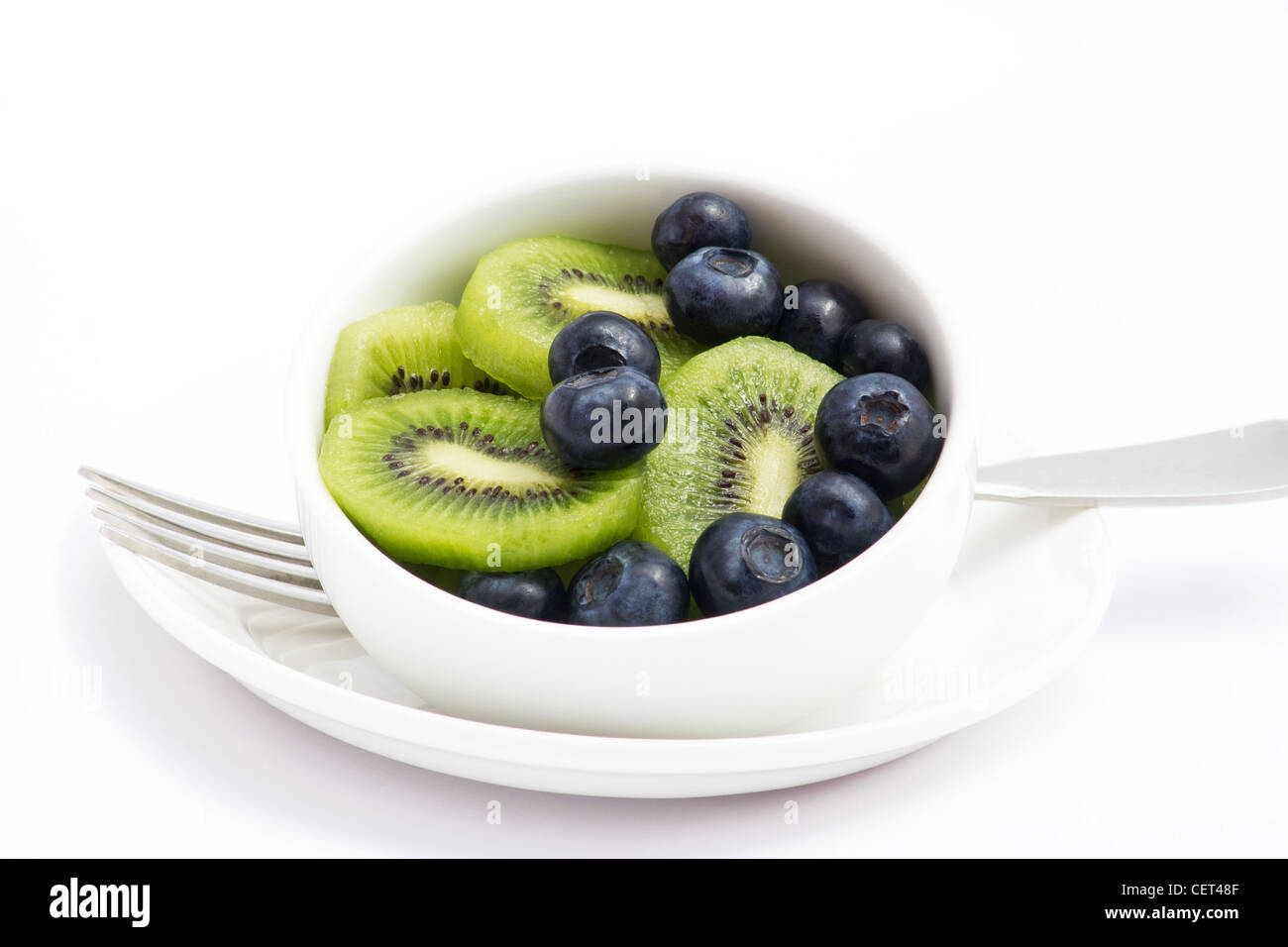 Sliced kiwi and blueberries in a white bowl on white background Stock Photo