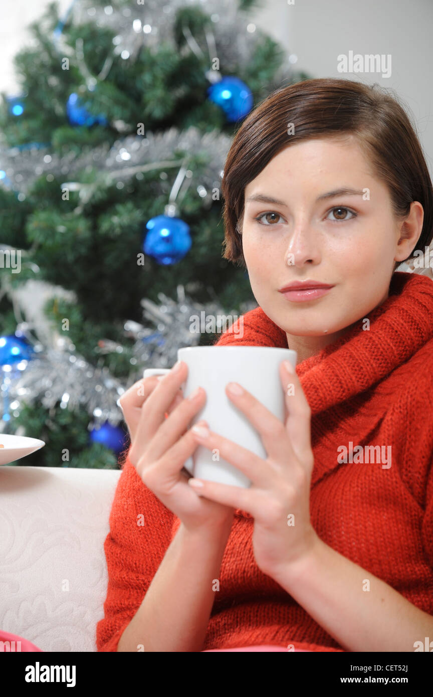 Female Short Brunette Hair Wearing A Red Jumper Sitting On White Sofa