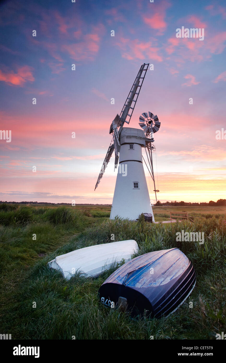 Sunrise over upturned boats by Thurne Mill standing at the entrance to Thurne Dyke on the Norfolk Broads. Stock Photo