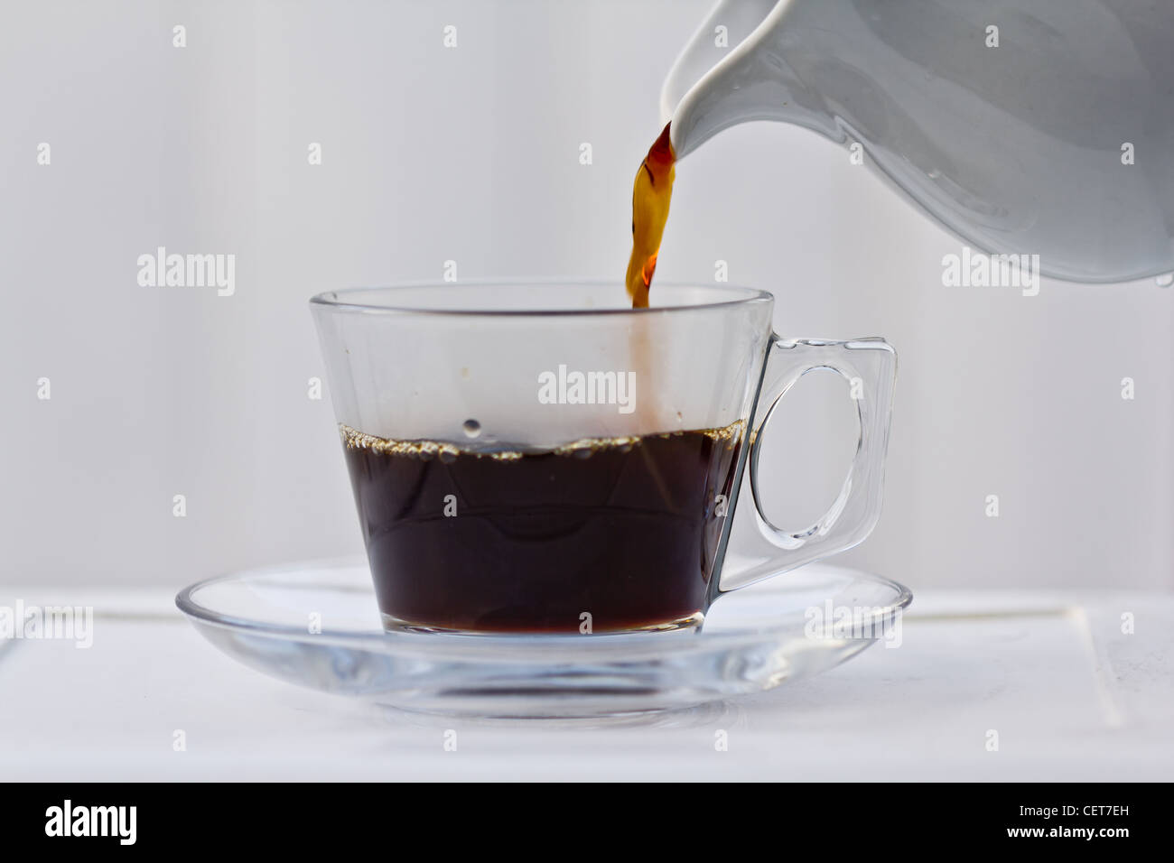 Pouring coffee into a half full clear cup with a saucer. Stock Photo