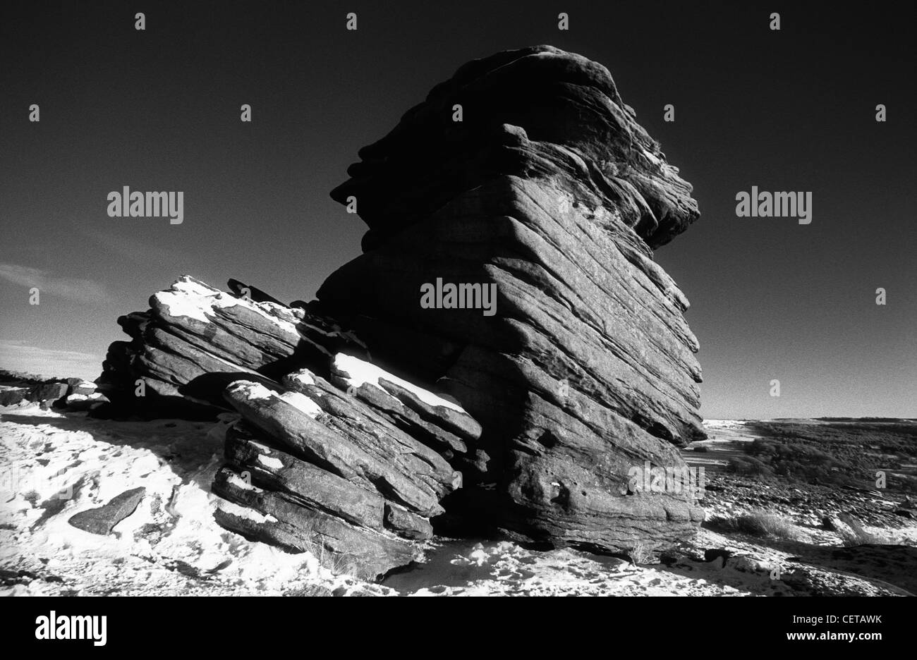 Black and white landscape of dramatic, rugged gritstone rocks covered in snow near Hathersage, Derbyshire in the Peak District. Stock Photo
