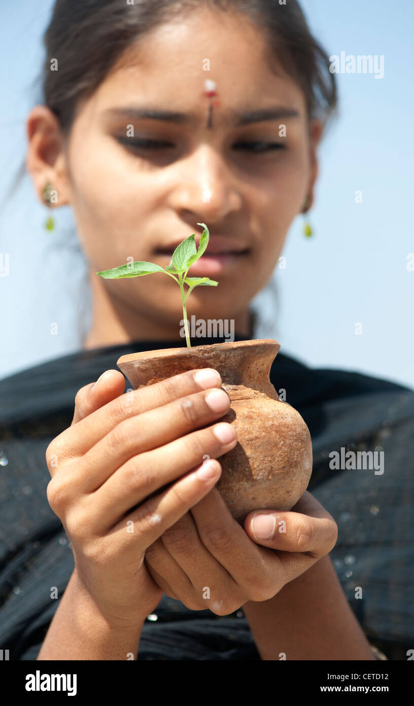 Indian teenage girl holding a plant seedling in a clay pot. India Stock