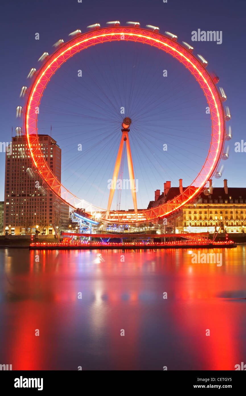 The London Eye with Red Nose Day lighting reflected in the Thames. The London Eye can carry 800 passengers per revolution - equi Stock Photo
