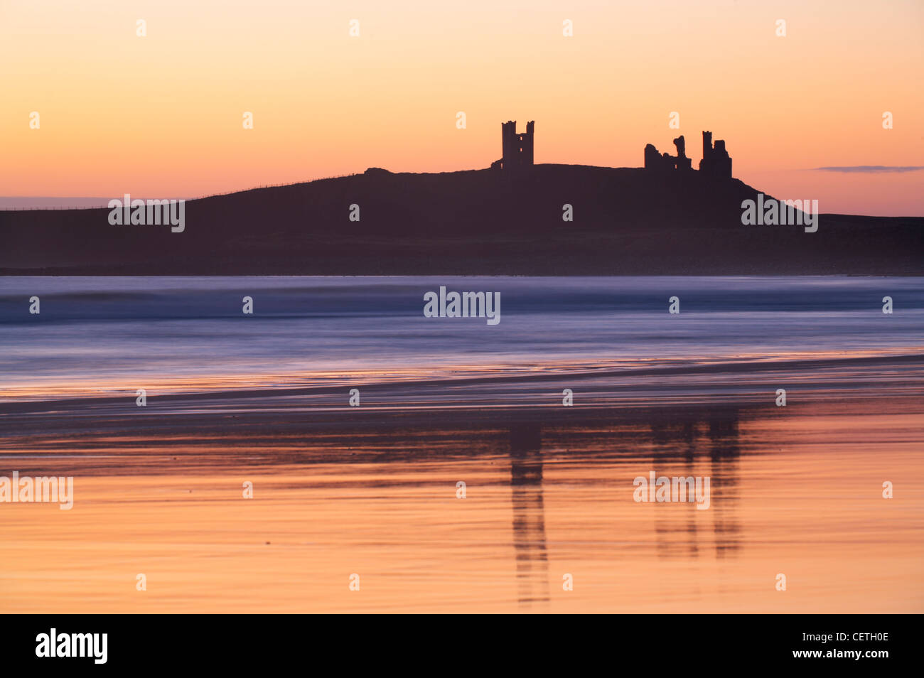 Dunstanburgh Castle at sunrise. Perched high on a cliff, Dunstanburgh Castle is now largely ruinous although it rated at one tim Stock Photo