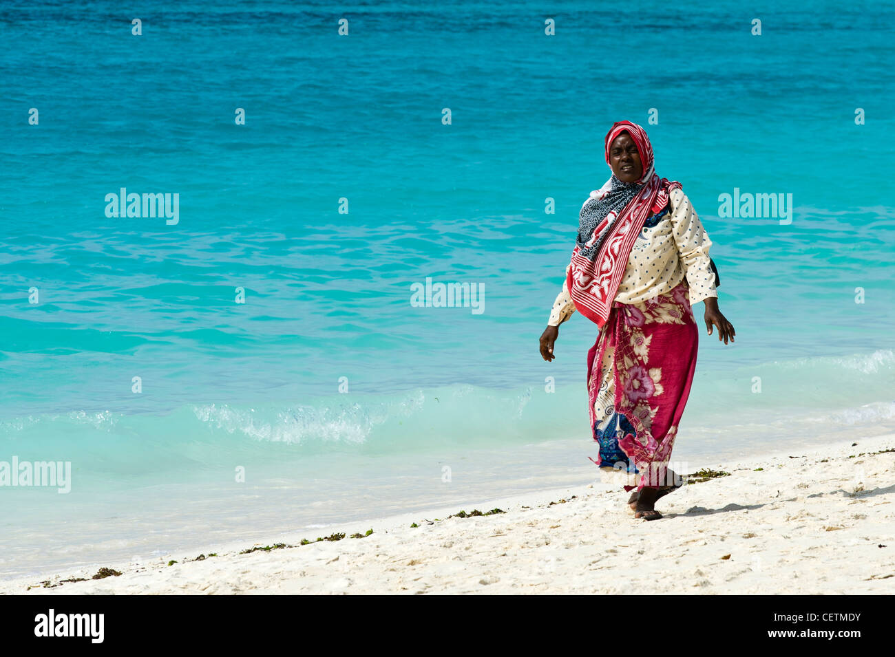 Woman in traditional dress walking along the beach in Kendwa Rocks north coast of Zanzibar Stock Photo