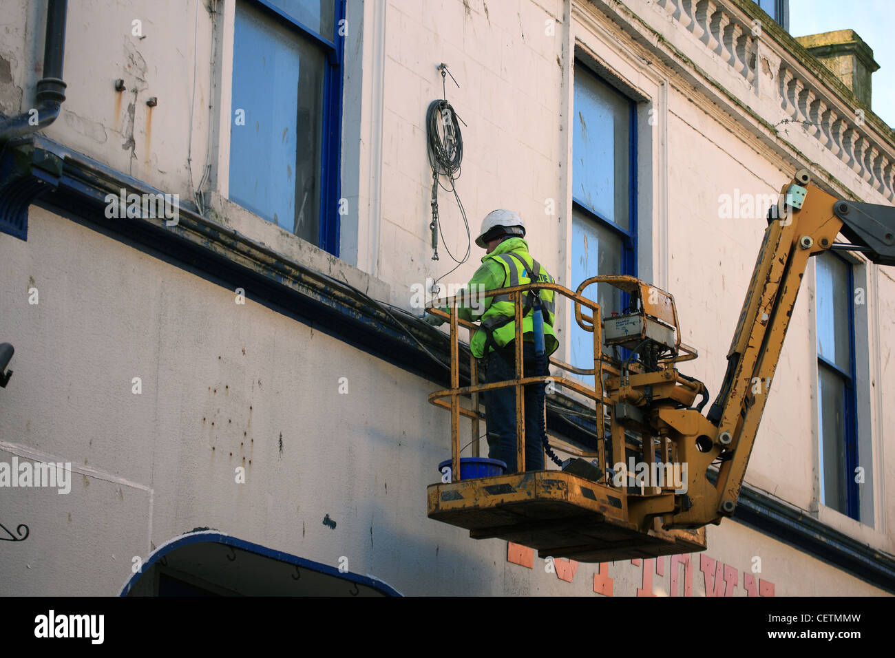 Workman wearing safety harness and hard hat on a crane hoist in the