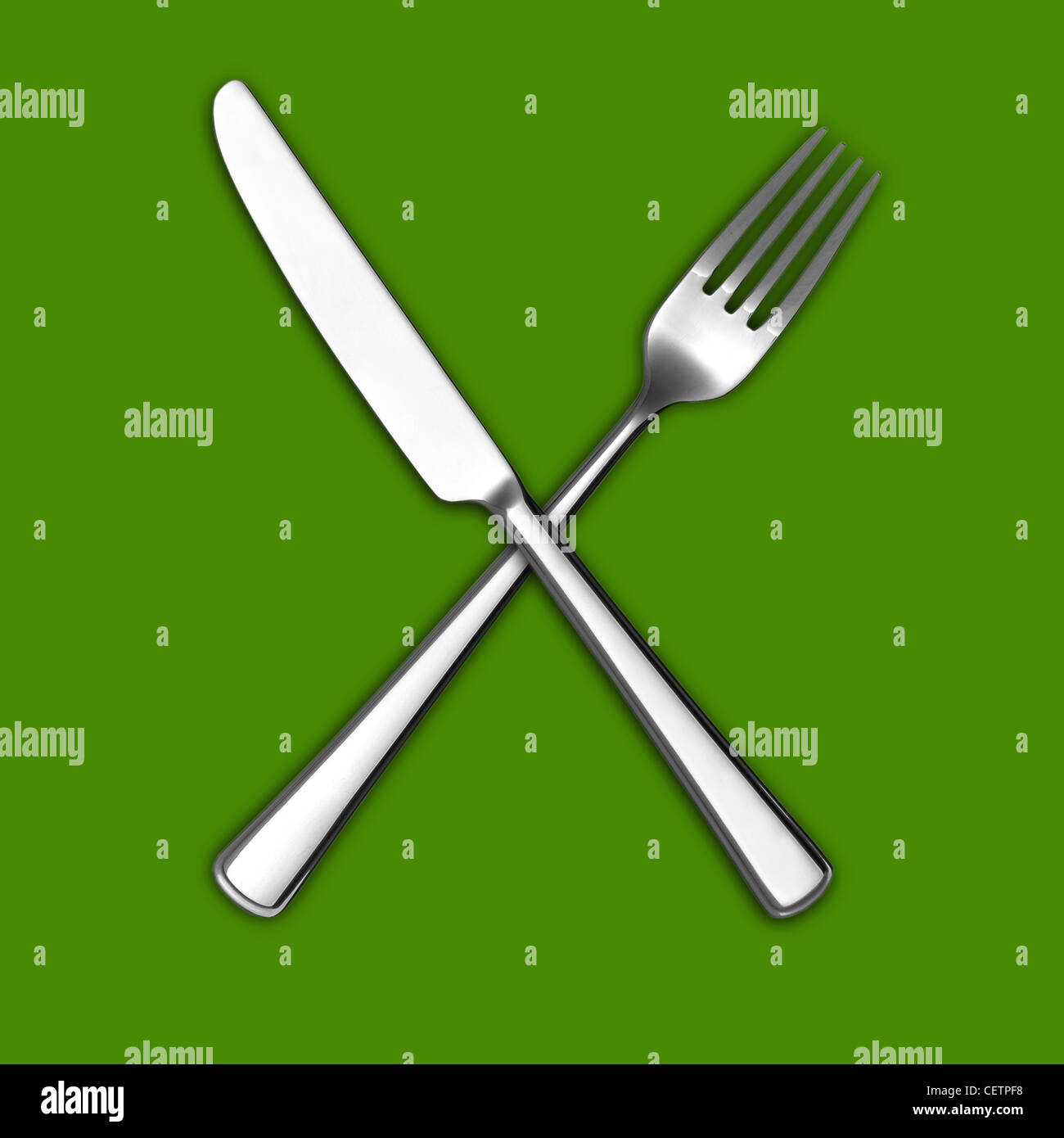 A still life shot of a knife and fork crossed on a green ...