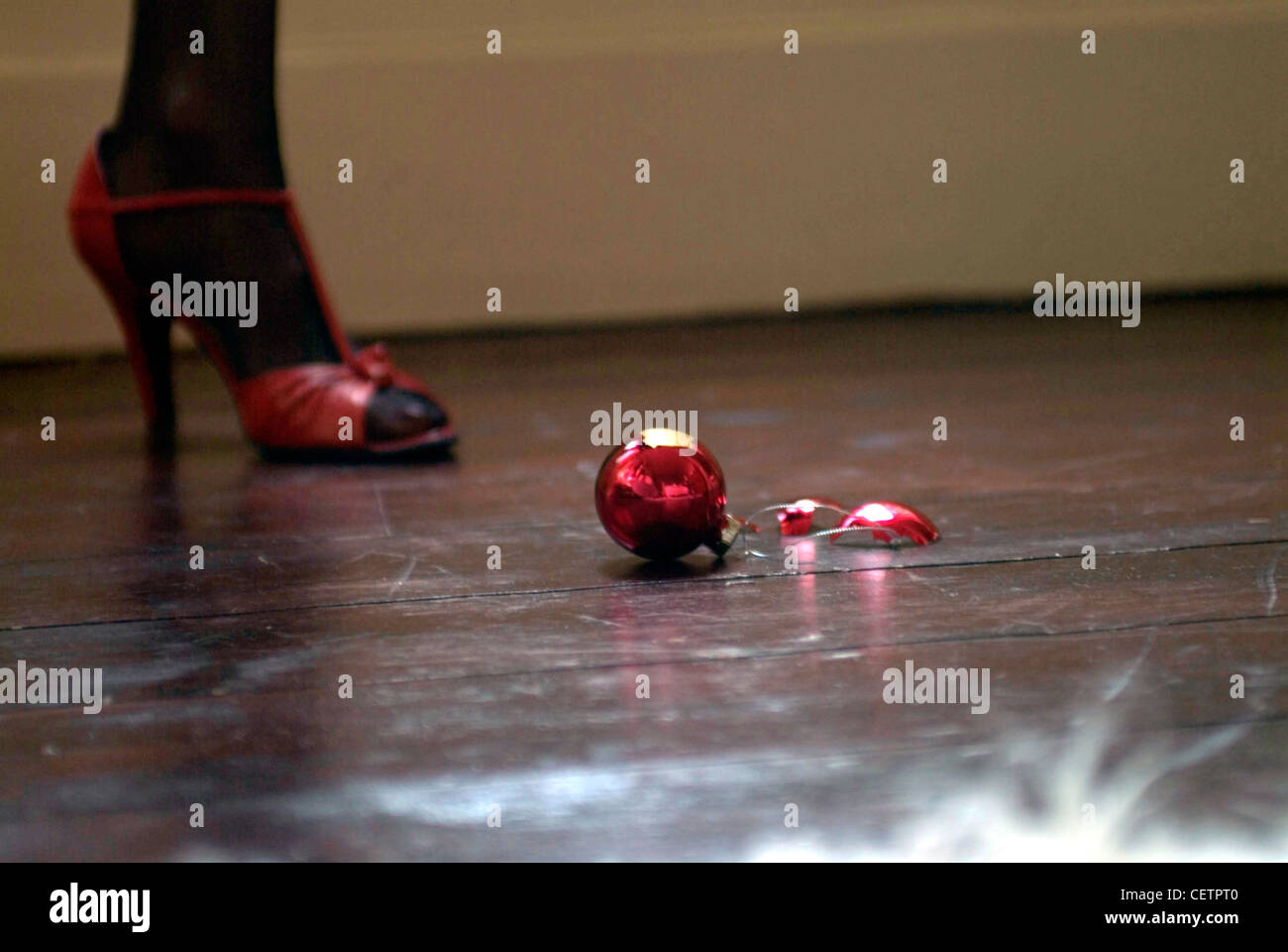 Cropped foot of female wearing black tights and red high heeled shoes strap at ankle, broken red bauble on wood floin Stock Photo