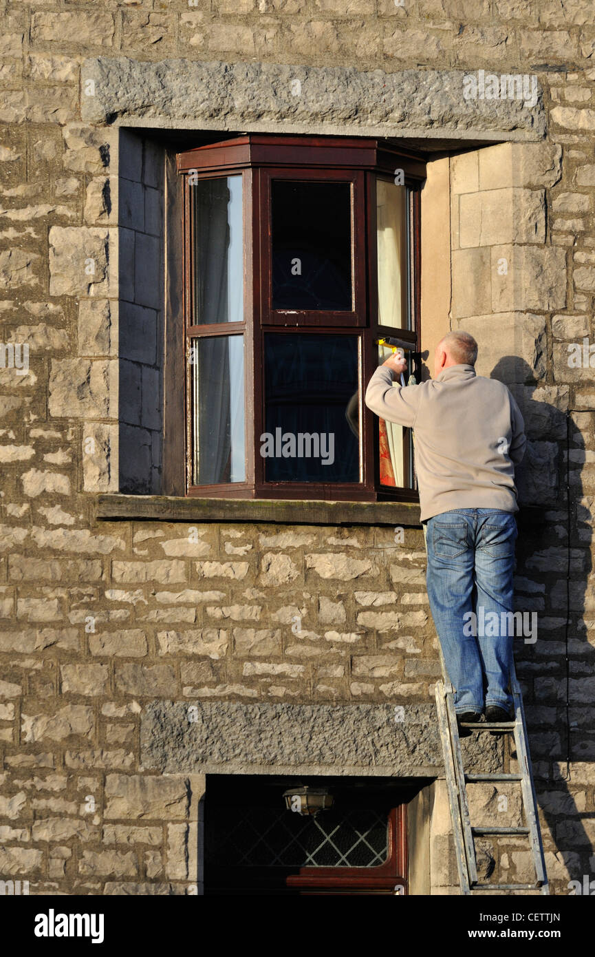 Man on ladder cleaning house windows. Lound Street, Kendal, Cumbria