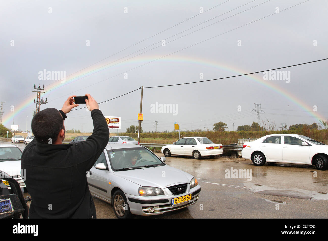 Cars pull over while the drivers look and photograph a full arc rainbow. Photographed in Israel Stock Photo