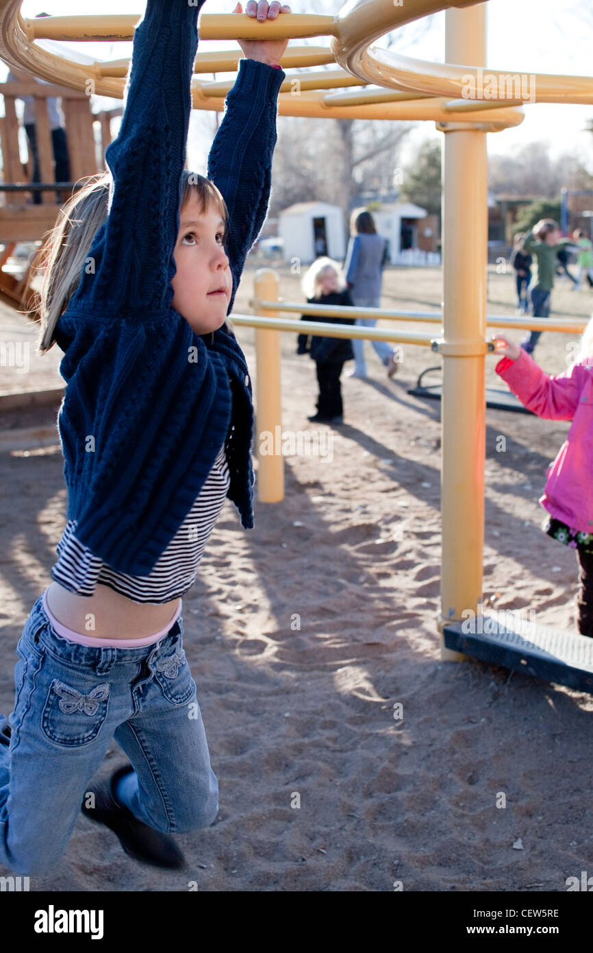 Five year old girl trying to hold herself up on the monkey bars on a playground. Stock Photo