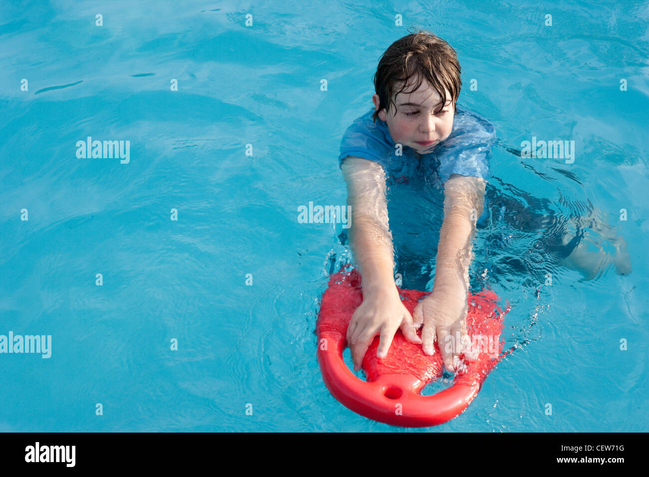 Twelve year old boy floats in swimming pool with a red floatation