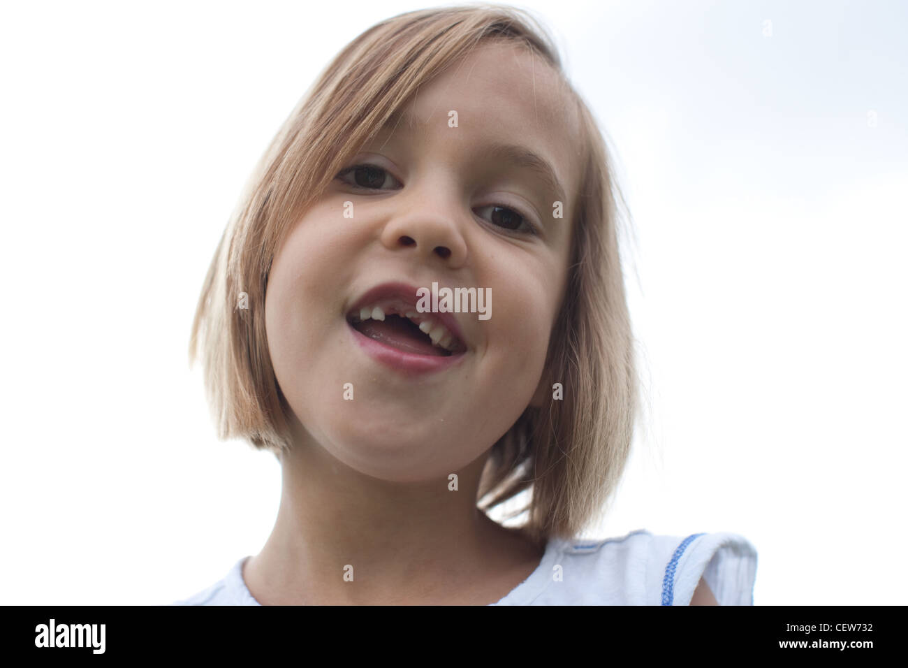 Six year old smiling with large gap, missing front teeth, sky in background. Stock Photo