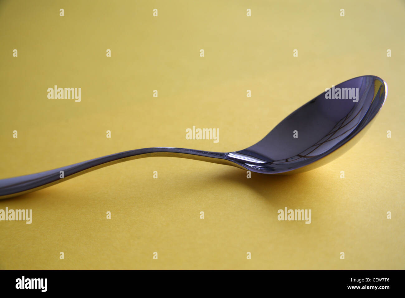 Silver soup spoon on yellow background Stock Photo