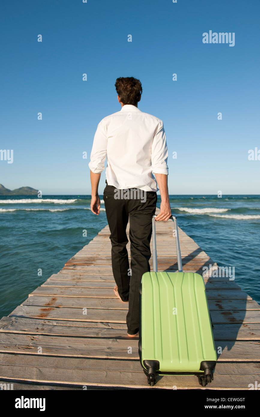 Man pulling luggage and walking on pier, rear view Stock Photo Alamy