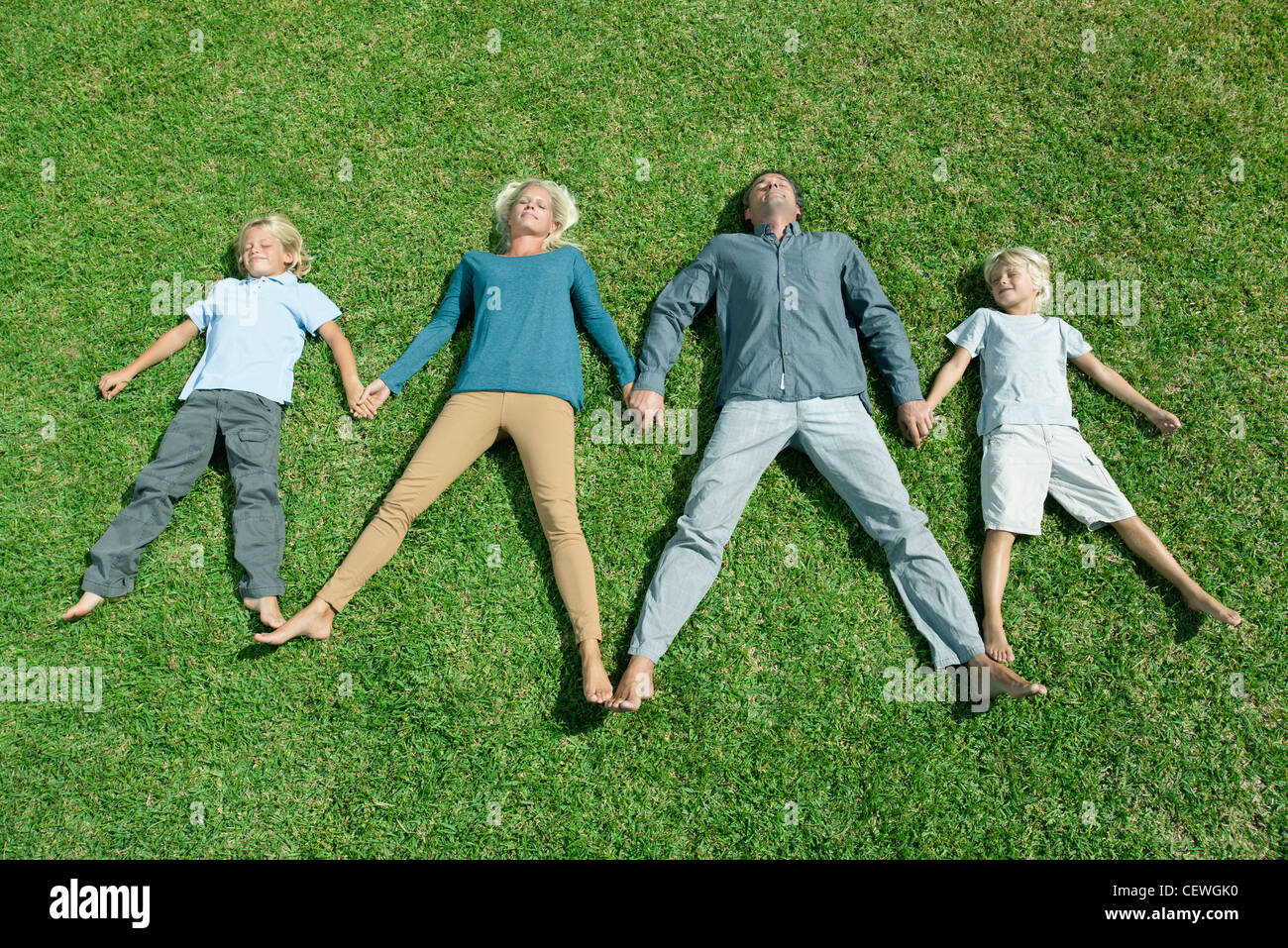 Family with two children lying side by side hand in hand on lawn, high angle view Stock Photo