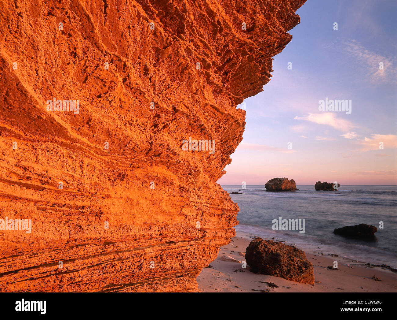 Sunset glows on cliff at Fingal Beach with the ocean in the background ...