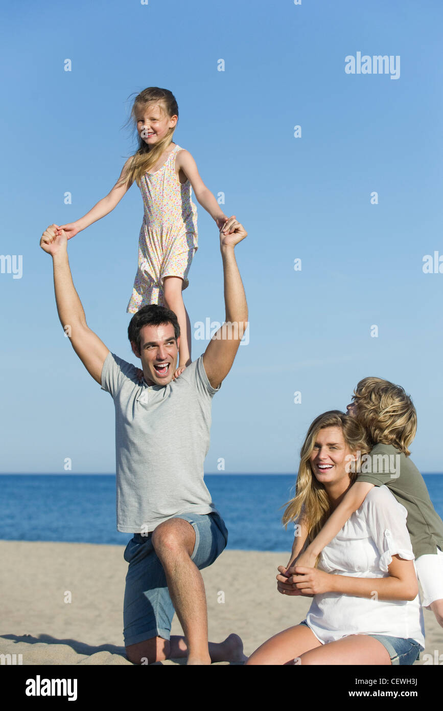 Family playing together at the beach, girl standing on her father's shoulders Stock Photo