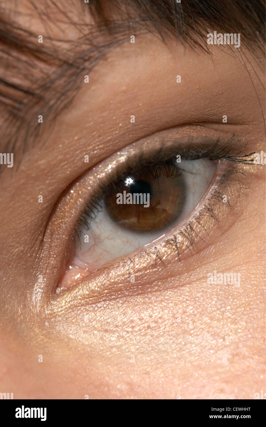 Close up eye of female wearing metallic gold eyeshadow, looking straight to camera Stock Photo