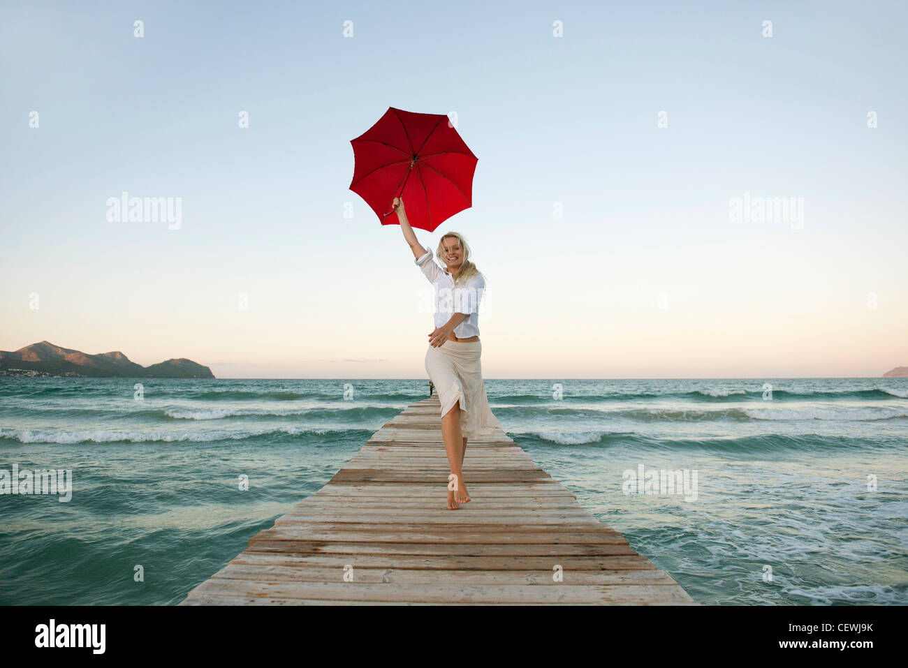 Young woman jumping on pier holding umbrella Stock Photo