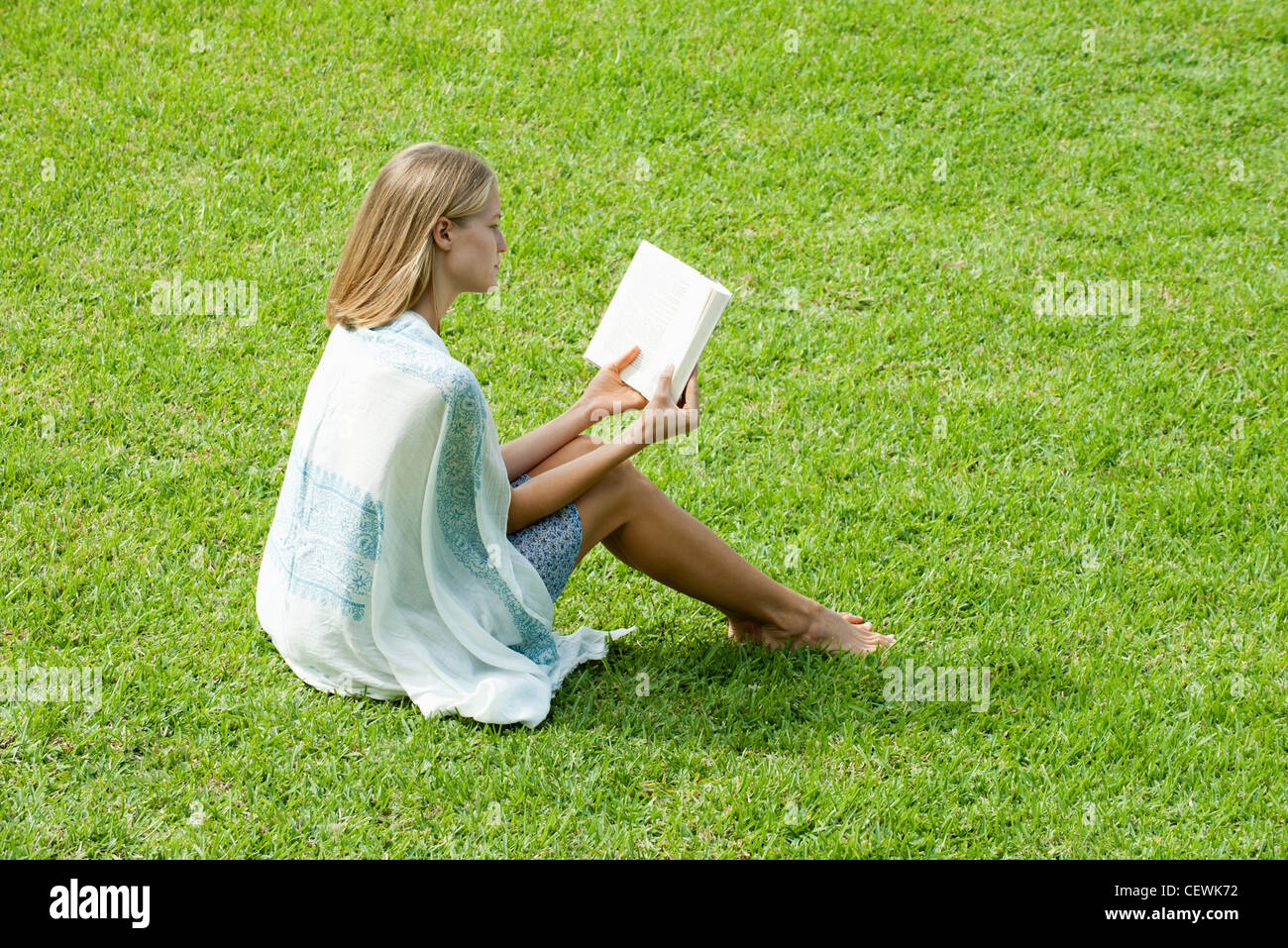 Young woman sitting on grass reading book Stock Photo