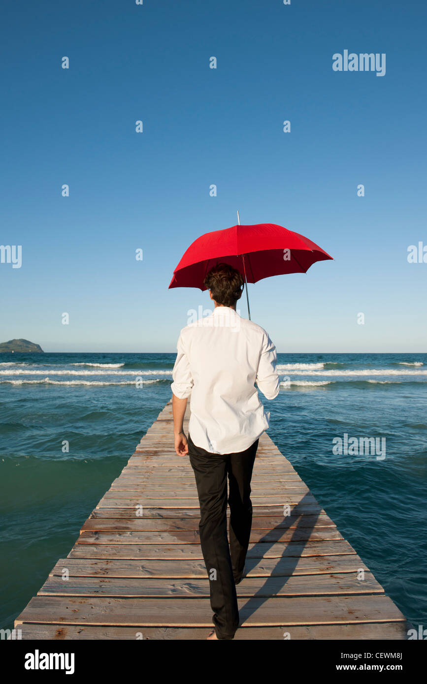 Man walking on pier with red umbrella, rear view Stock Photo Alamy