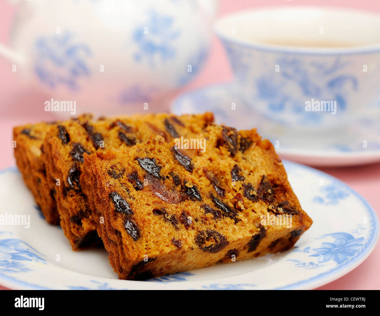 A white and blue patterned plate filled slices of fruit cake, a blue and white patterned teapot and cup and saucer in the Stock Photo