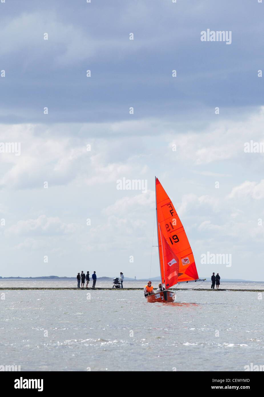 One red sailing boat on the marine lake, West Kirby, Wirral, UK, with people walking around the lake wall in the background Stock Photo